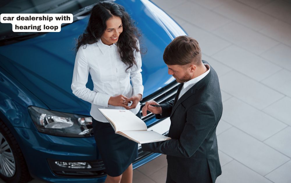 Car dealership showroom featuring prominent Hearing Loop Support signage at the service desk with staff assisting customers