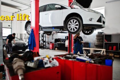 Red two-post car lift raising a vehicle in a workshop